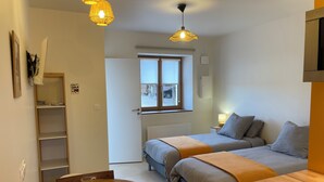 Quarto compacto com duas camas, uma mesa de madeira com dois copos e uma janela com vista para a rua.