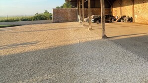 Um espaço ao ar livre coberto, com chão de cascalho, vigas de metal e luzes de corda.