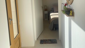 Um corredor leva a um quarto com uma cama, uma mesa de cabeceira, uma luminária e um espelho na parede.