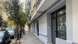 Eine schmale Stadtstraße mit parkenden Autos und einem Gebäude mit großen Fenstern und einem Eingang.