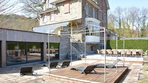A modern outdoor patio with sun loungers and a glass enclosure. - Villa in Coo Near Waterfalls With Pool (Stavelot)