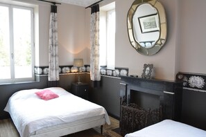 Ein Schlafzimmer mit zwei Betten, einem Spiegel, einem Kamin und einem Fenster mit Vorhängen.