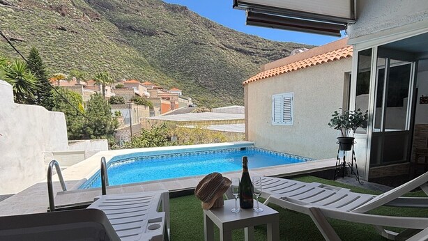 Un espace aménagé au bord de la piscine, avec une pelouse artificielle, des chaises longues et une table sur laquelle se trouvent une bouteille et des verres.