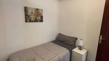 A small, neatly arranged bedroom with a bed, a nightstand, a lamp, and a painting on the wall.