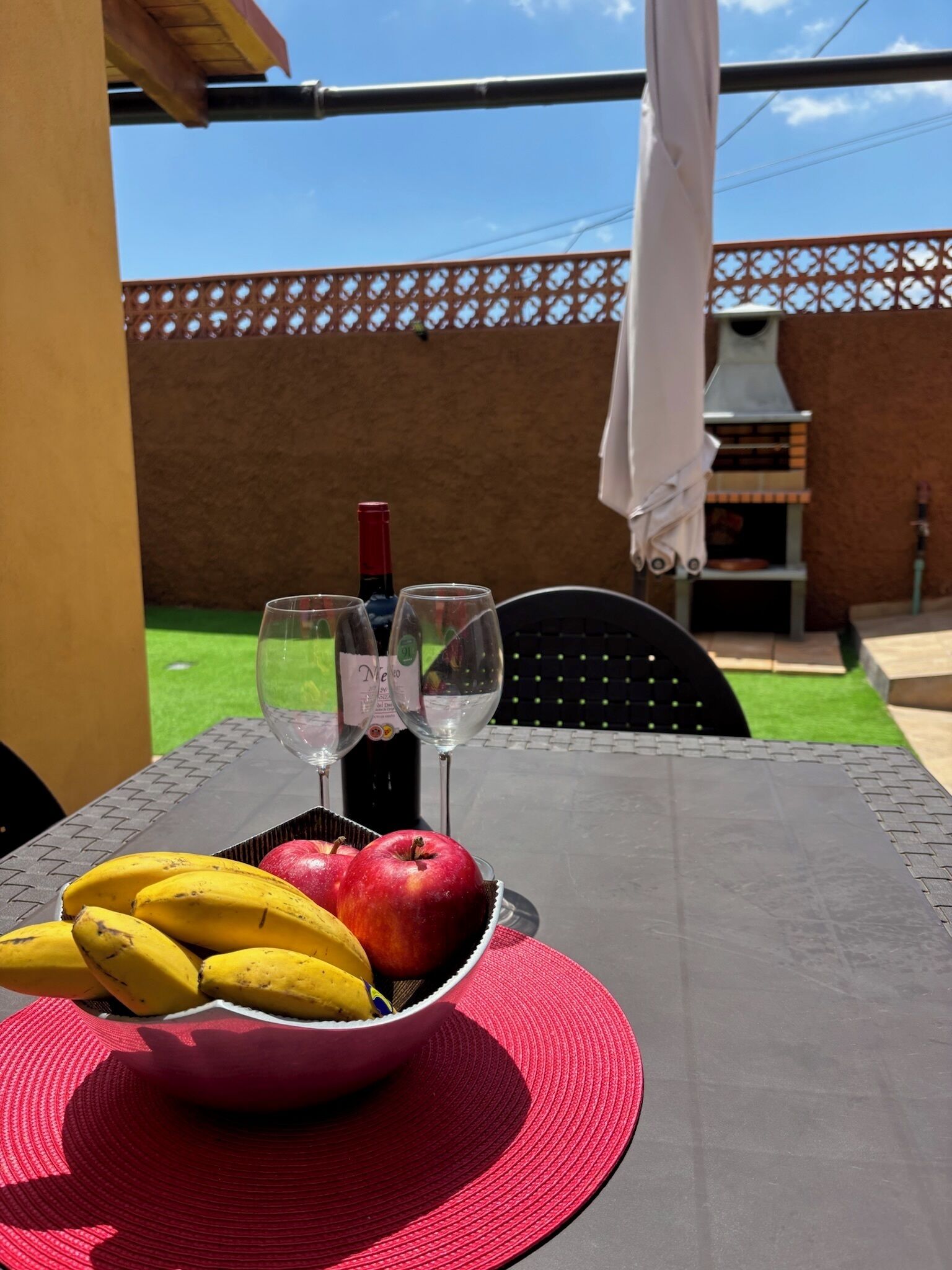 A table with a bowl of fruit, two wine glasses, and a bottle of wine.