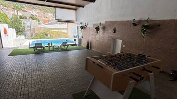An indoor recreational area with a foosball table, a pool table, and a view of a residential neighborhood.