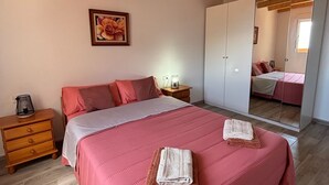 Une chambre avec un grand lit, des poutres apparentes en bois au plafond, une armoire, une table de chevet et un tableau encadré au mur.
