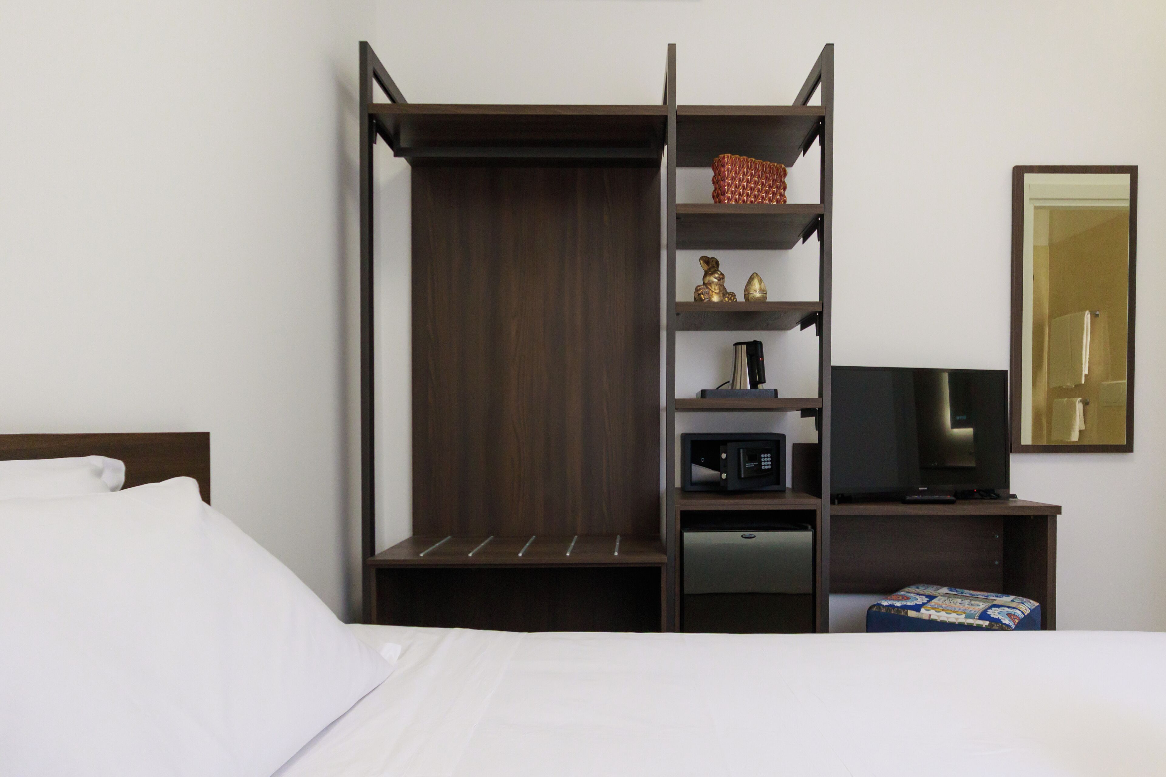 A hotel room with a bed, a TV, a microwave, and a small shelf with decorative items.