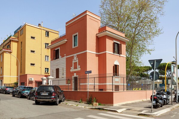 A multi-story building with a red and yellow facade, parked cars, and a motorcycle on the street. - Villa Aurora Rooms (Rome)