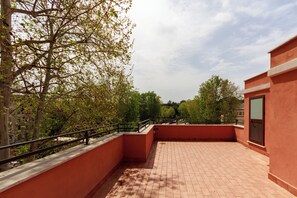 A rooftop terrace with a brick floor, surrounded by trees and a red building. - Villa Aurora Rooms (Rome)