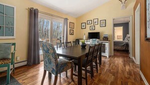 A dining area with a wooden table and chairs, a window with curtains, and a view of trees outside.