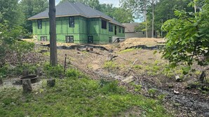 Een groen gebouw in aanbouw met een schuin dak, omringd door bomen en een gazon.