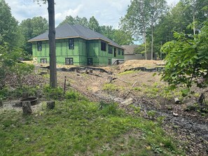 A green building under construction with a sloped roof, surrounded by trees and a grassy area. - Summerwood Cottage (South Haven)