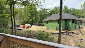 Een groen huis in aanbouw met een houten terras op de voorgrond.