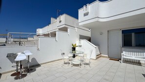 Une terrasse sur le toit avec une table et des chaises, un pot de fleurs et un banc blanc.