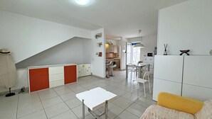 Una cocina moderna con armarios blancos, un comedor con sillas blancas y una escalera que sube a otro nivel.