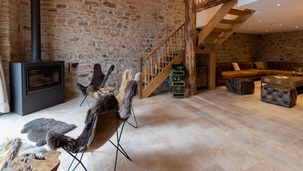 A rustic interior with a stone wall, a fireplace, a wooden staircase, and a leather sofa. - Farmhouse in Ardennes Near Coo Waterfalls (Trois-Ponts)