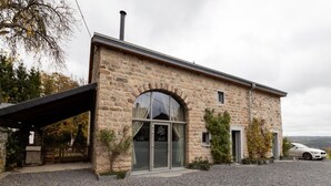 A stone building with a large arched entrance, a covered outdoor area, and a parked car. - Farmhouse in Ardennes Near Coo Waterfalls (Trois-Ponts)