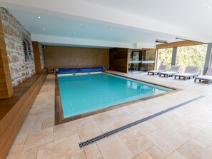 A large indoor swimming pool with a stone wall on one side, a wooden floor, and a seating area with sun loungers. - Farmhouse in Ardennes Near Coo Waterfalls (Trois-Ponts)