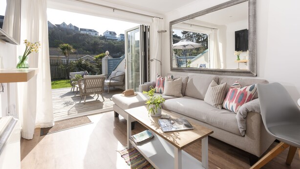 Un salon spacieux avec un grand canapé, une table basse et un téléviseur. Une porte-fenêtre coulissante donne accès à un balcon aménagé avec du mobilier d’extérieur.