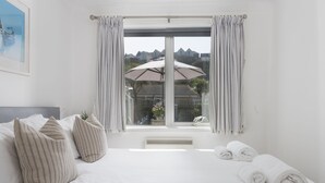 Une chambre avec un grand lit, des oreillers à rayures, une fenêtre avec des rideaux et une vue sur les maisons à l’extérieur.