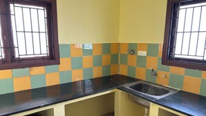 A kitchen with a black countertop, a sink, and a window with bars. - Shiva Nest (Tiruchirappalli)