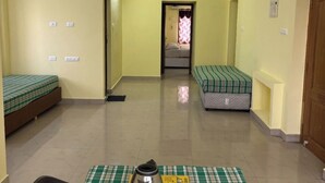 A room with two single beds, a dining table with a tray of cups and a kettle, and a ceiling fan. - Shiva Nest (Tiruchirappalli)