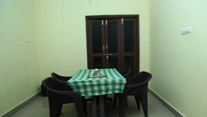 A small dining area with a square table covered by a green and white checkered tablecloth, four black chairs, and a wooden cabinet with glass doors behind the table. - Shiva Nest (Tiruchirappalli)