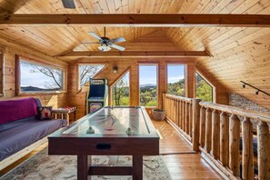A wooden interior with a foosball table, a sofa, and a view of the outdoors.