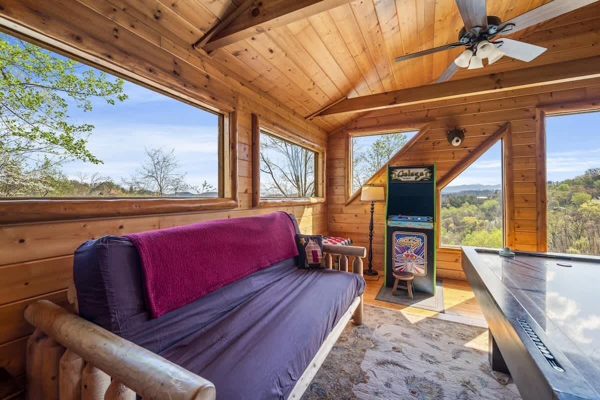 Ein Holzblockbau-Innenraum mit einer Couch, einem Billardtisch und Blick ins Freie.