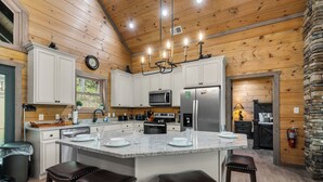 A kitchen with a central island, white cabinets, stainless steel appliances, and a stone accent wall.