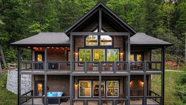 A multi-level wooden cabin with balconies, large windows, and a hot tub on the ground floor.
