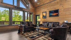 A cozy living room with a wooden ceiling, large windows, a sofa set, a coffee table, and a rug with animal prints.