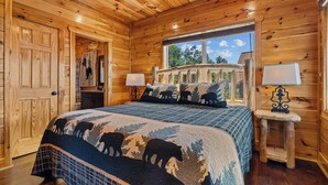 A wooden cabin bedroom with a large bed, two bedside tables with lamps, and a window with a view of trees. - Long range sunset views from Hot Tub, free attractions, Resort pool (Sevierville)