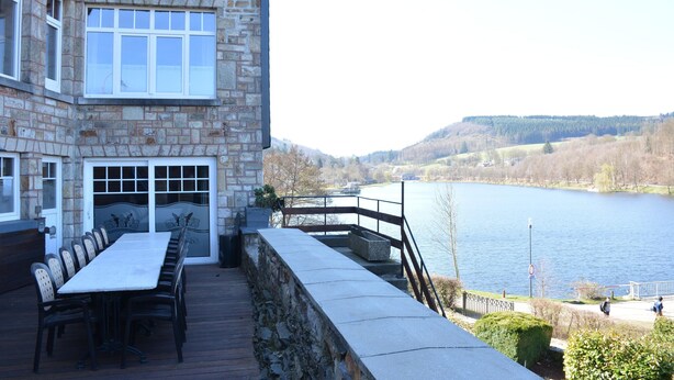 A stone building with a long table and chairs outside, overlooking a lake and hills. - Villa in Vielsalm With Lake Views and Pool (Vielsalm)