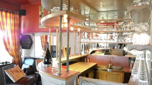 A bar area with shelves of glassware, a bar counter, and a seating area with a chair and a table. - Villa in Vielsalm With Lake Views and Pool (Vielsalm)