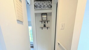 A narrow hallway with wooden flooring, a white door with a framed picture, and a small shelf with a decorative item.
