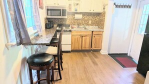 A compact kitchen with a dining area, wooden cabinets, and a window with curtains.