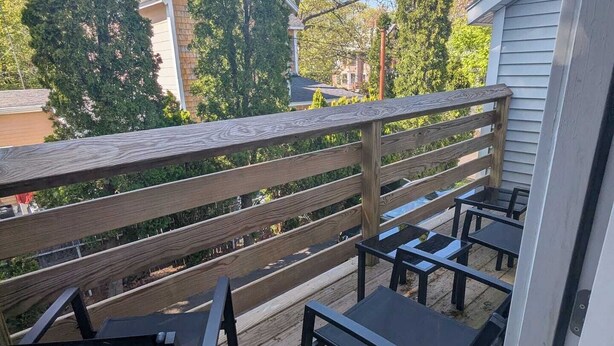 A wooden deck with outdoor furniture, a railing, and a view of surrounding trees and houses.