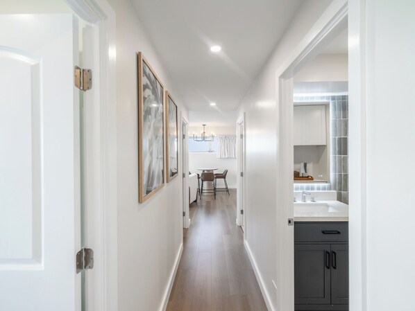 A hallway with a dining area, a kitchen with a large mirror, and framed artwork on the walls.