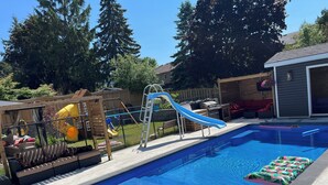 A backyard with a swimming pool, a slide, and a playset. - Detached home with heated saltwater pool 45 minutes from Toronto (Whitby)