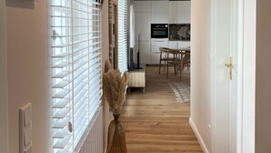 A hallway with white blinds, a radiator, a wooden floor, and a dining area with a table and chairs.