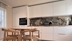 A modern kitchen with white cabinets, a marble backsplash, and a wooden dining table with chairs.