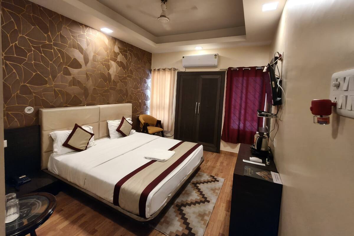 A hotel room with a bed, a chair, a desk, an air conditioning unit, and a wardrobe.