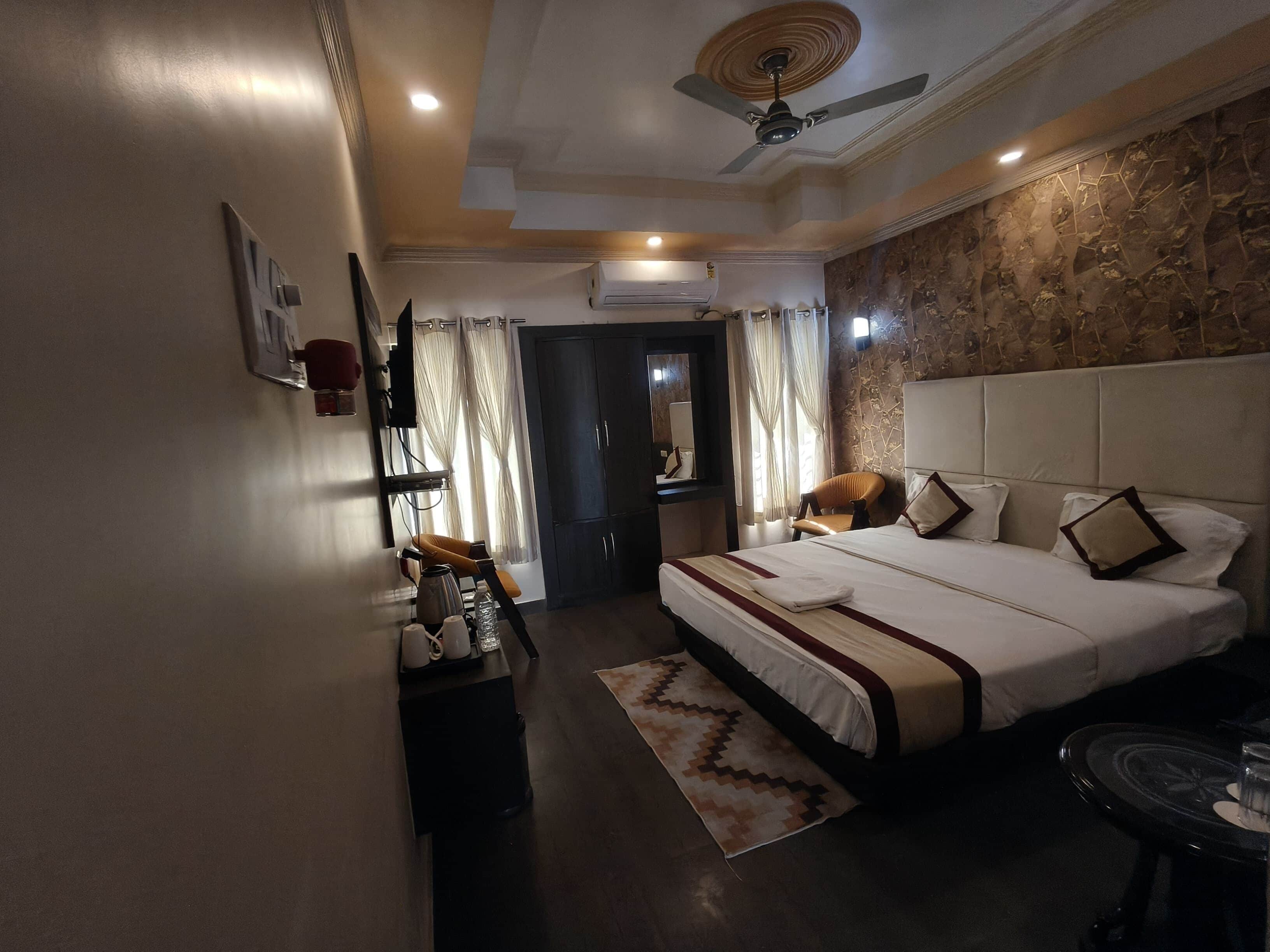 A hotel room with a bed, a desk, a chair, a ceiling fan, and a stone wall.