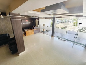 Un espace d’accueil d’hôtel comprenant un comptoir de réception, un panneau fixé au mur et une porte vitrée donnant sur l’extérieur.