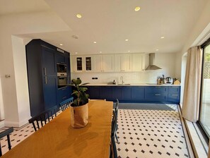 A modern kitchen with dark blue cabinets, a wooden dining table, and a potted plant. - Chic Property With Backyard Near Emirates Stadium (Greater London)