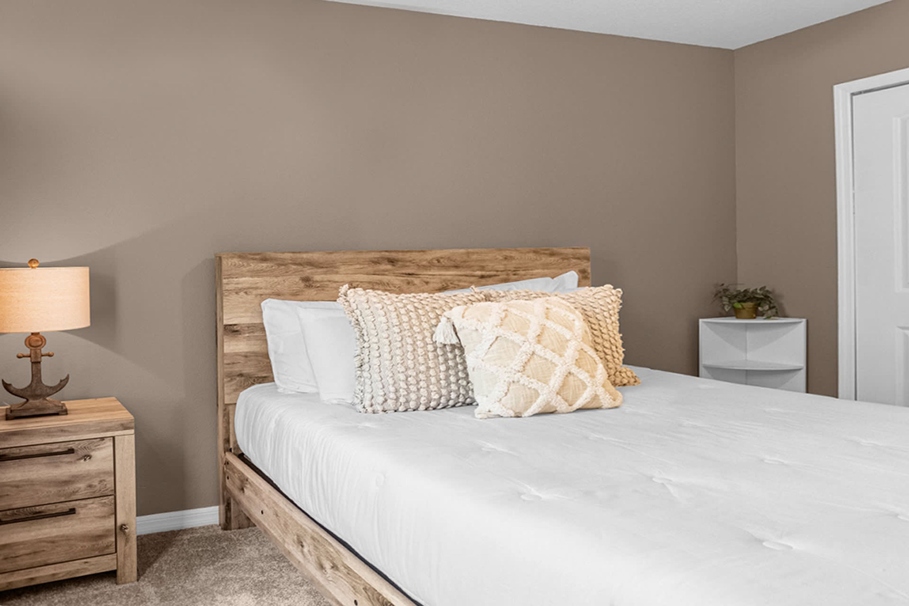 Una camera da letto con testiera in legno, copripiumino bianco e diversi cuscini decorati.