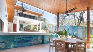 A modern house with a covered patio, a dining area, and a colorful mosaic pool.