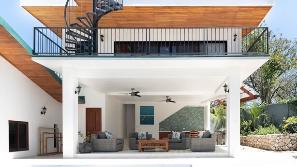 A modern two-story house with a covered outdoor seating area, a pool, and a spiral staircase.